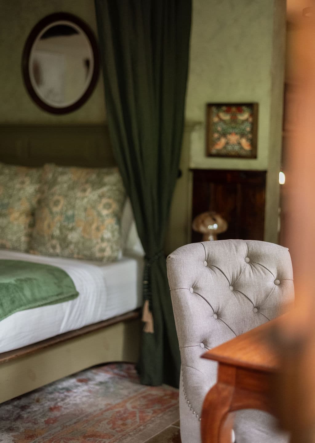 A cozy room featuring a bed with patterned pillows, a grey upholstered chair, and green curtains.