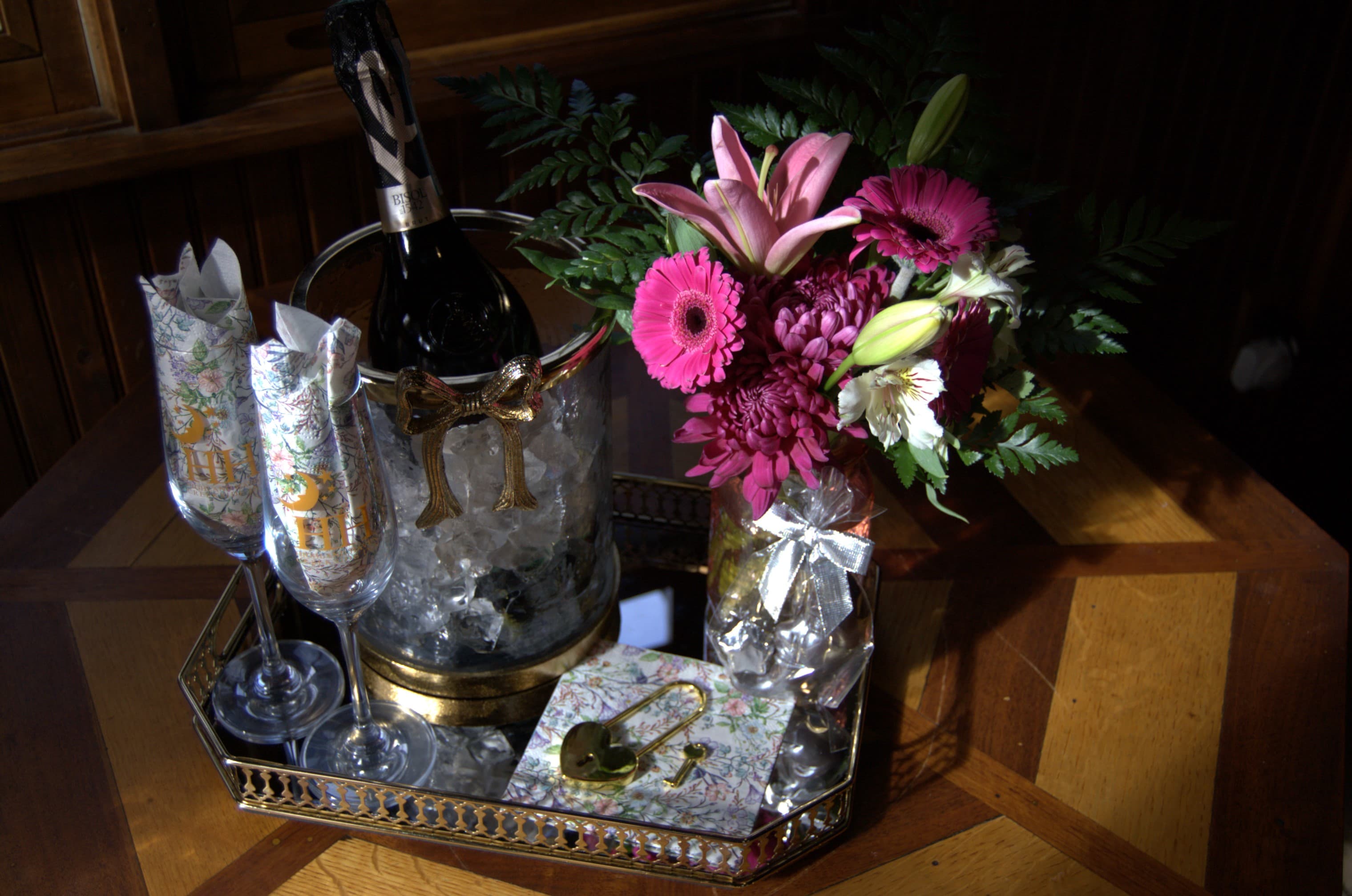 A tray displays champagne in an ice bucket, elegant glasses, and a vibrant floral arrangement.