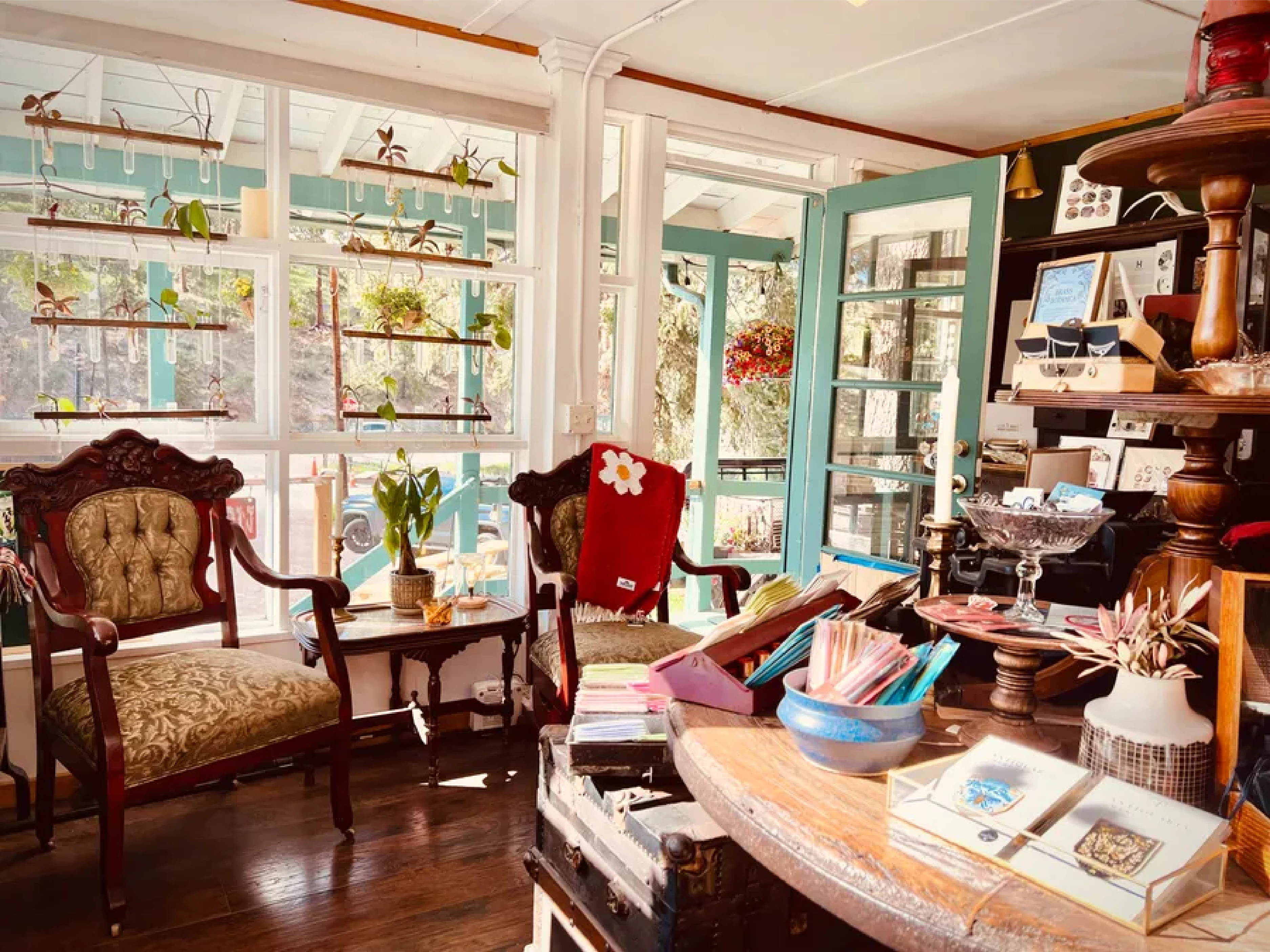 A cozy interior featuring vintage chairs, plants, and a wooden table with assorted items.