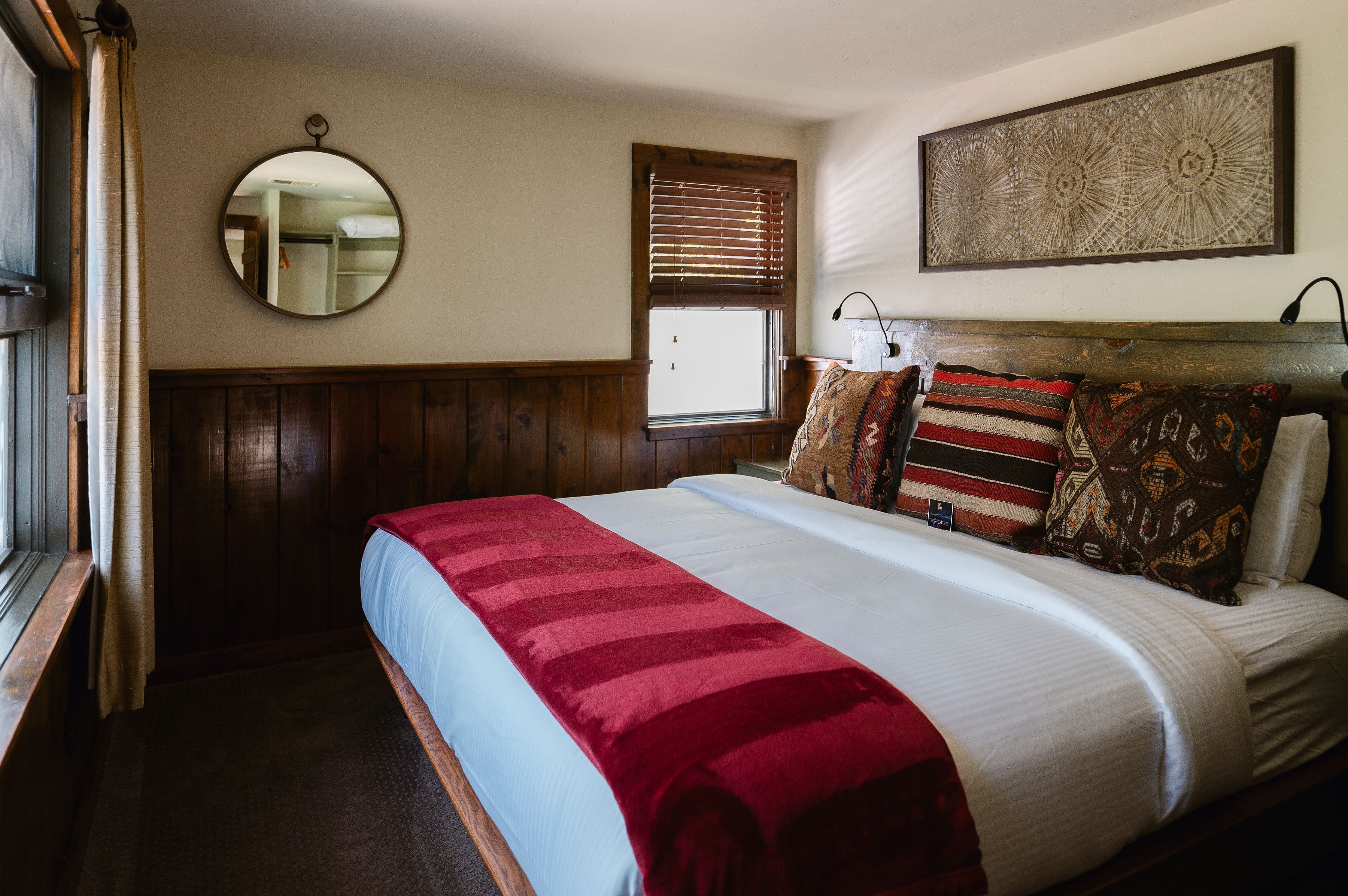 Cozy bedroom featuring a hardwood-paneled wall, a bed with decorative pillows, and a round mirror.