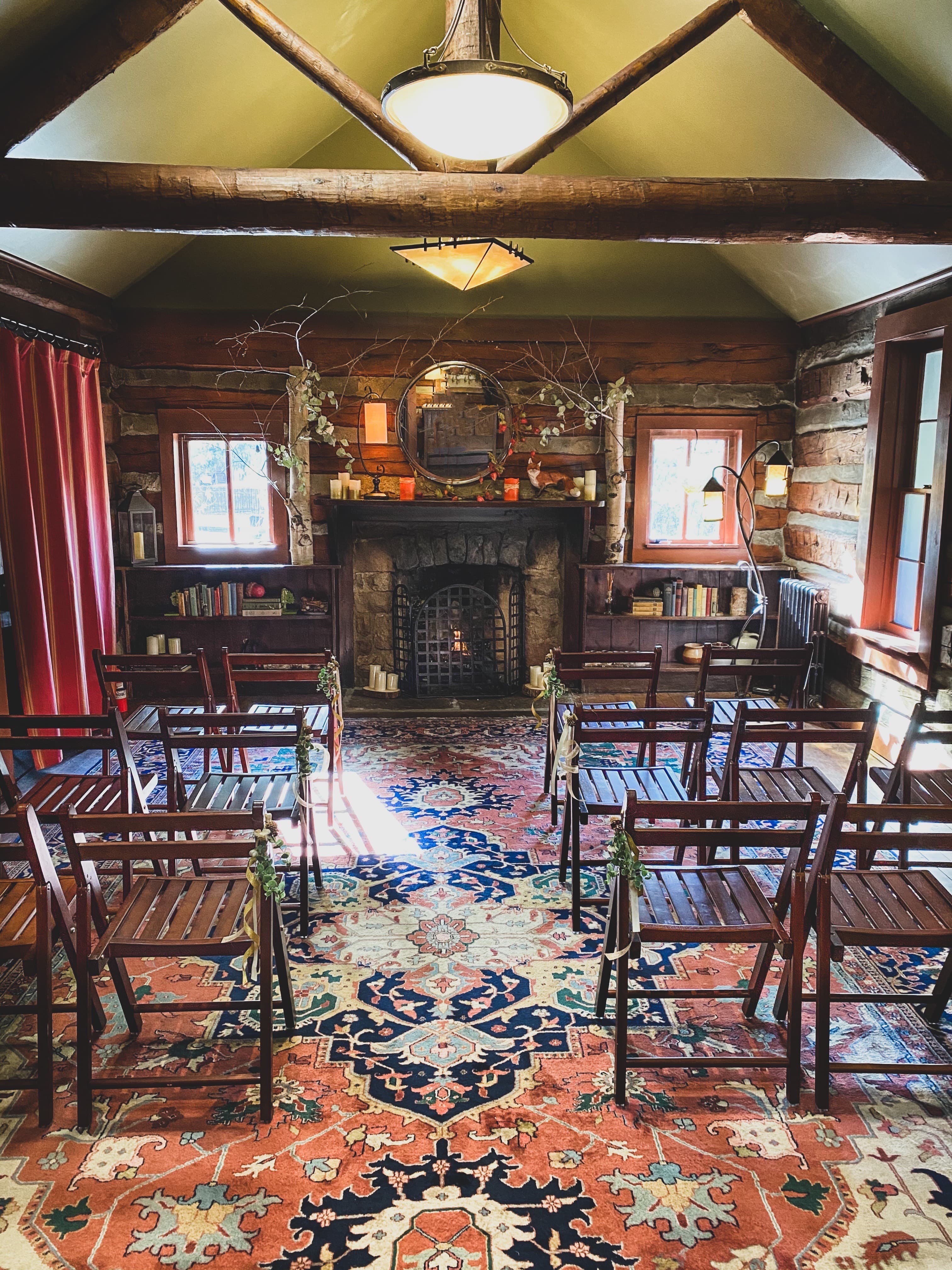 Cozy gathering space with wooden chairs, a stone fireplace, and a patterned rug.