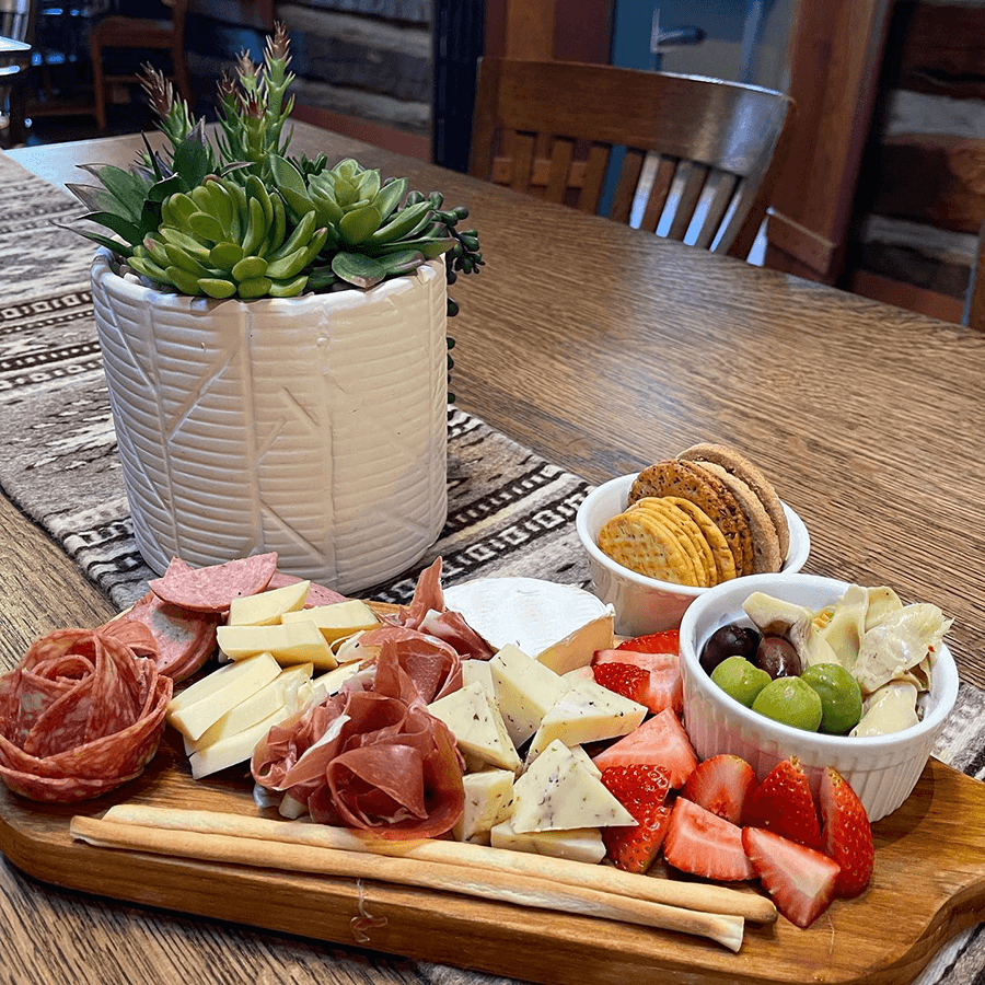 A charcuterie board featuring various meats, cheeses, strawberries, olives, and crackers, accompanied by a succulent centerpiece.