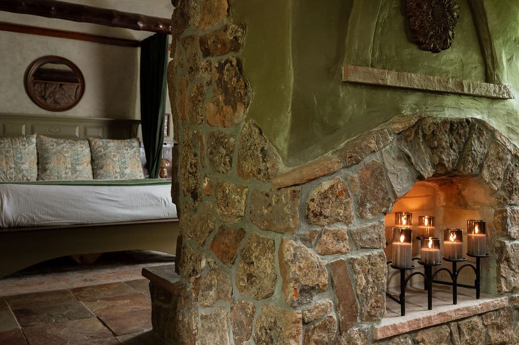 A cozy stone fireplace with candles, framed by a rustic bedroom setting.