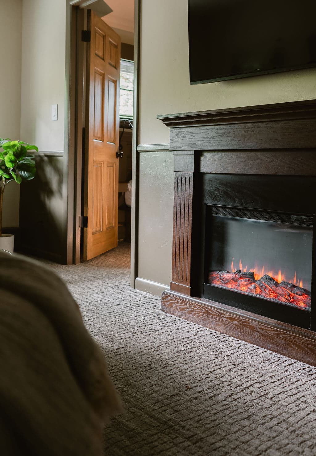 A cozy living space featuring an electric fireplace, plush carpet, and an open door leading to another room.