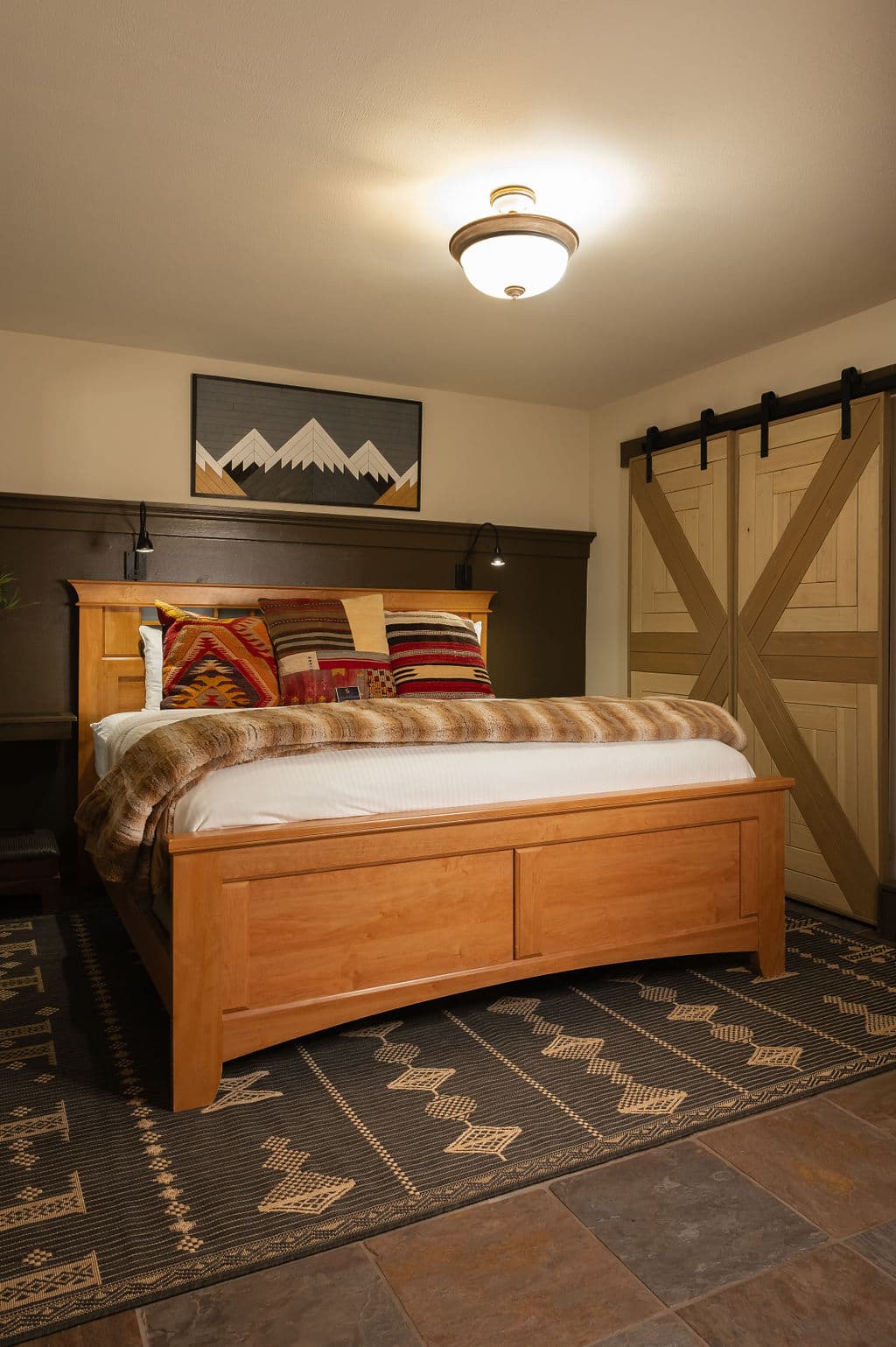 A cozy bedroom featuring a wooden bed with decorative pillows, a mountain-themed painting, and sliding barn doors.