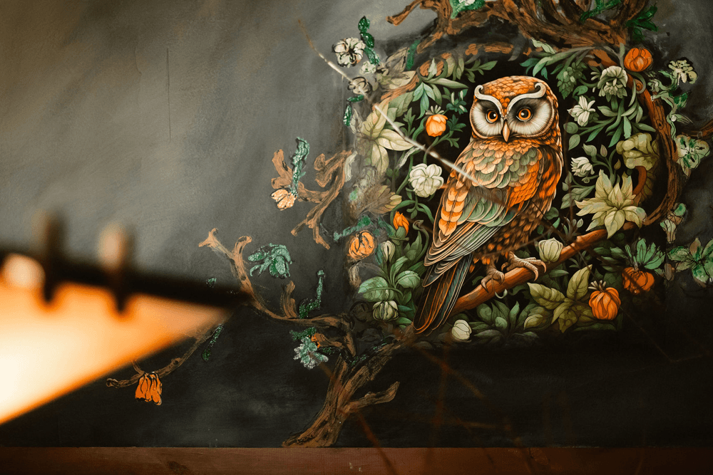 A colorful owl is painted amidst floral designs on a dark wall.