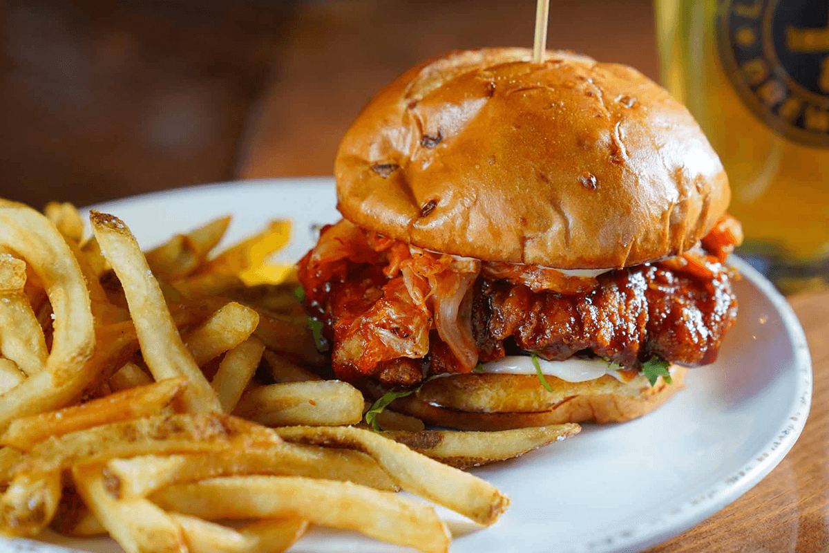 A spicy chicken sandwich with kimchi and mayonnaise served alongside golden French fries.