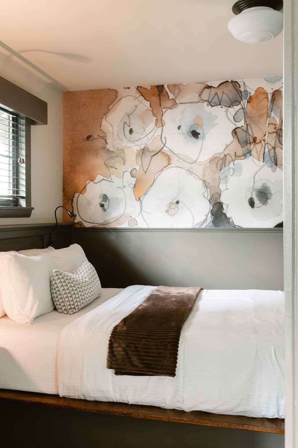 A cozy bedroom featuring a white bed, patterned pillow, and an artistic floral mural on the wall.