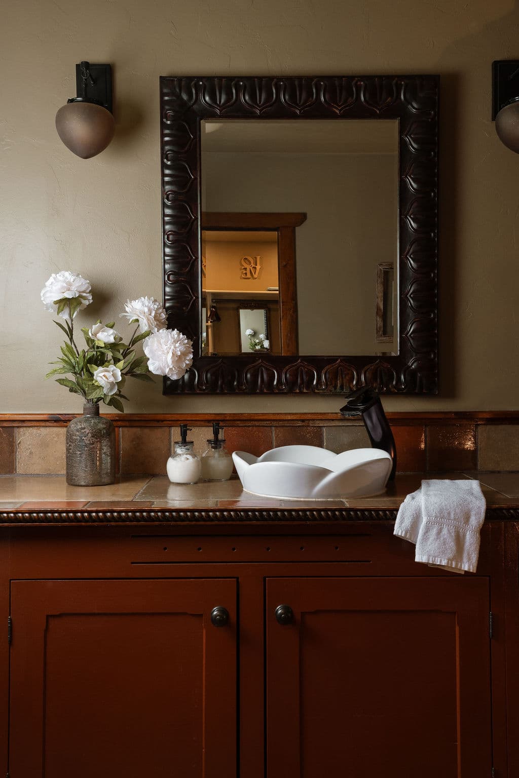 A stylish bathroom featuring a white sink, floral arrangement, and a large framed mirror.