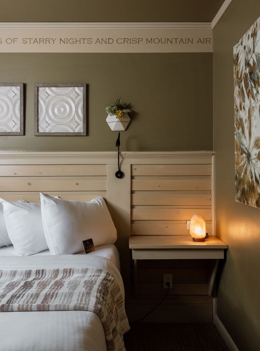 A cozy bedroom corner with a bed, decorative wall art, and a bedside table featuring a salt lamp.