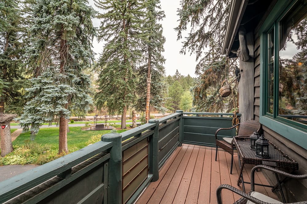 A cozy balcony with wicker chairs overlooks a lush forest of tall pine trees. The scene is serene and inviting, offering a peaceful natural retreat.