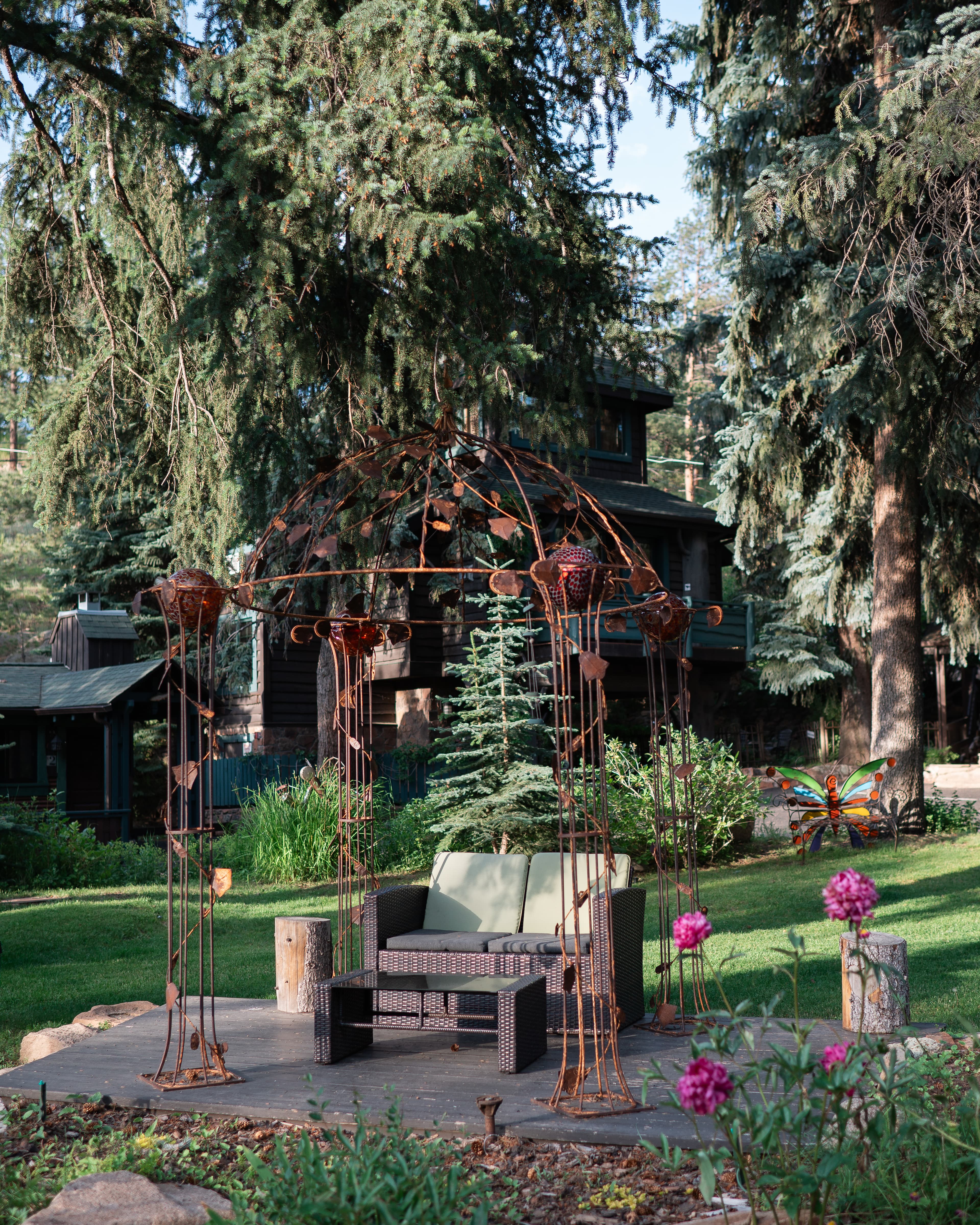 A decorative gazebo with a seating area is surrounded by greenery and flowers.