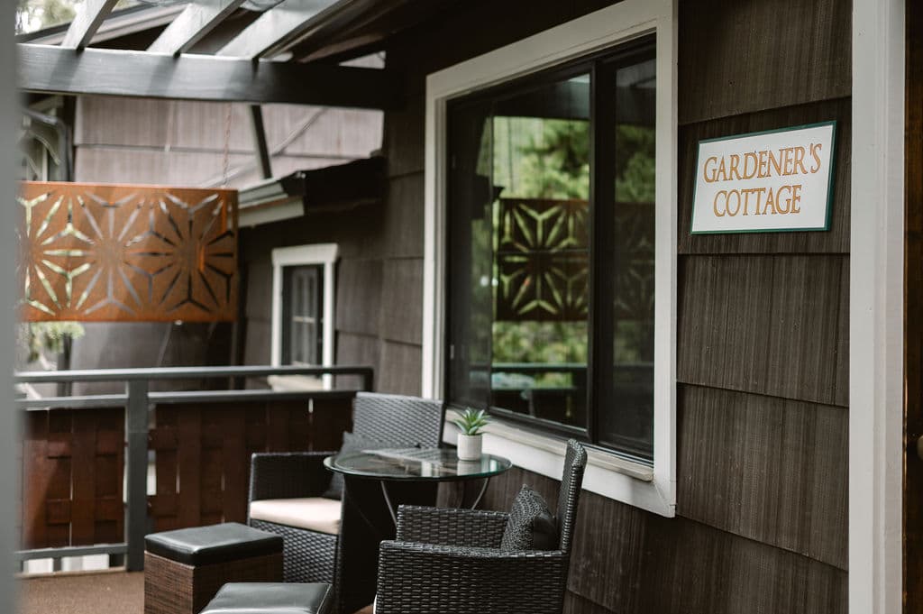Cozy patio with wicker furniture and a glass table outside "GARDENER'S COTTAGE." A warm, calm atmosphere with wood paneling and decorative screens.