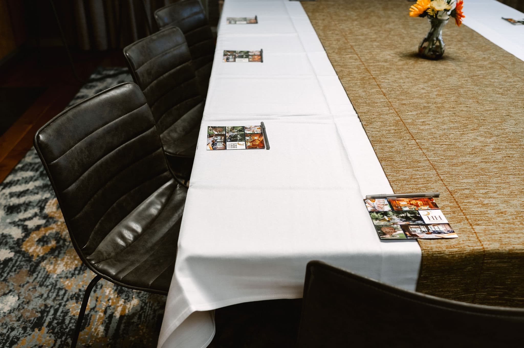 A long table set with a white tablecloth, black chairs, and decorative cards placed on top.