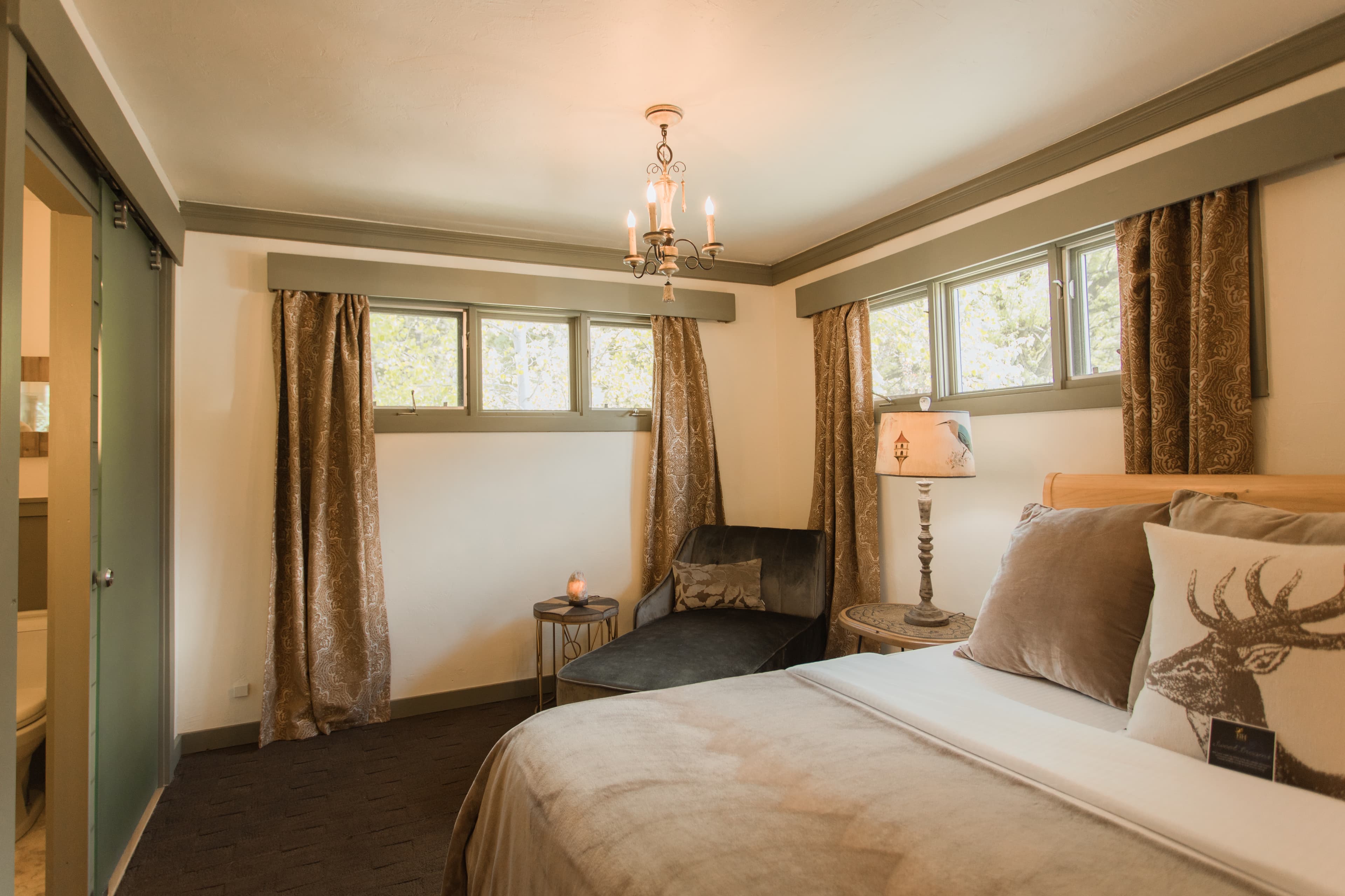 Cozy bedroom with a bed, plush chair, decorative pillows, and warm lighting.