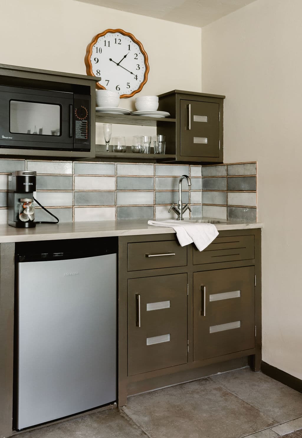 kitchenette with mini-fridge, microwave, coffee maker, dishes on shelves above metal sink.