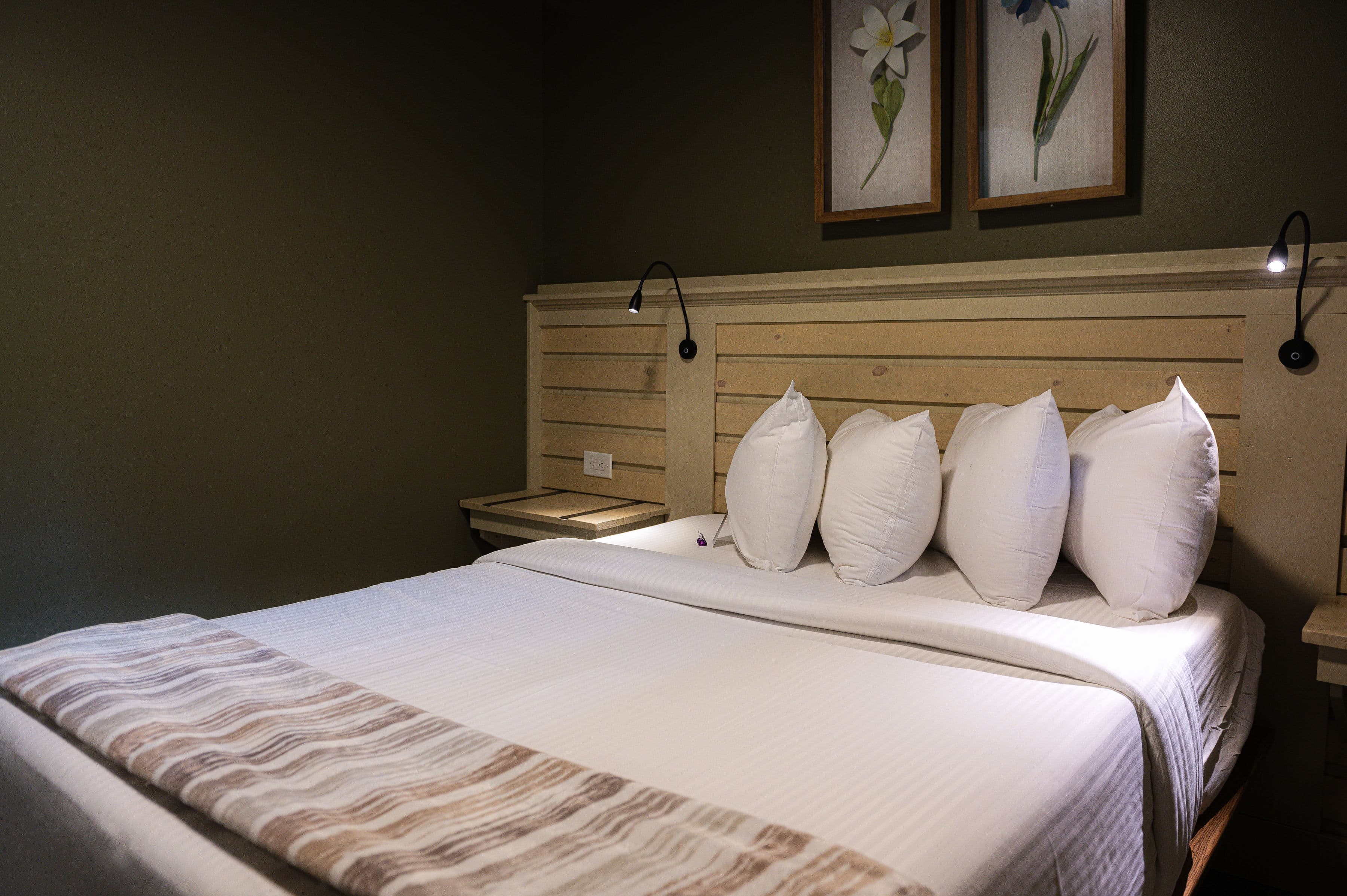 A neatly made bed with decorative pillows and a wooden headboard is set against a dark green wall.