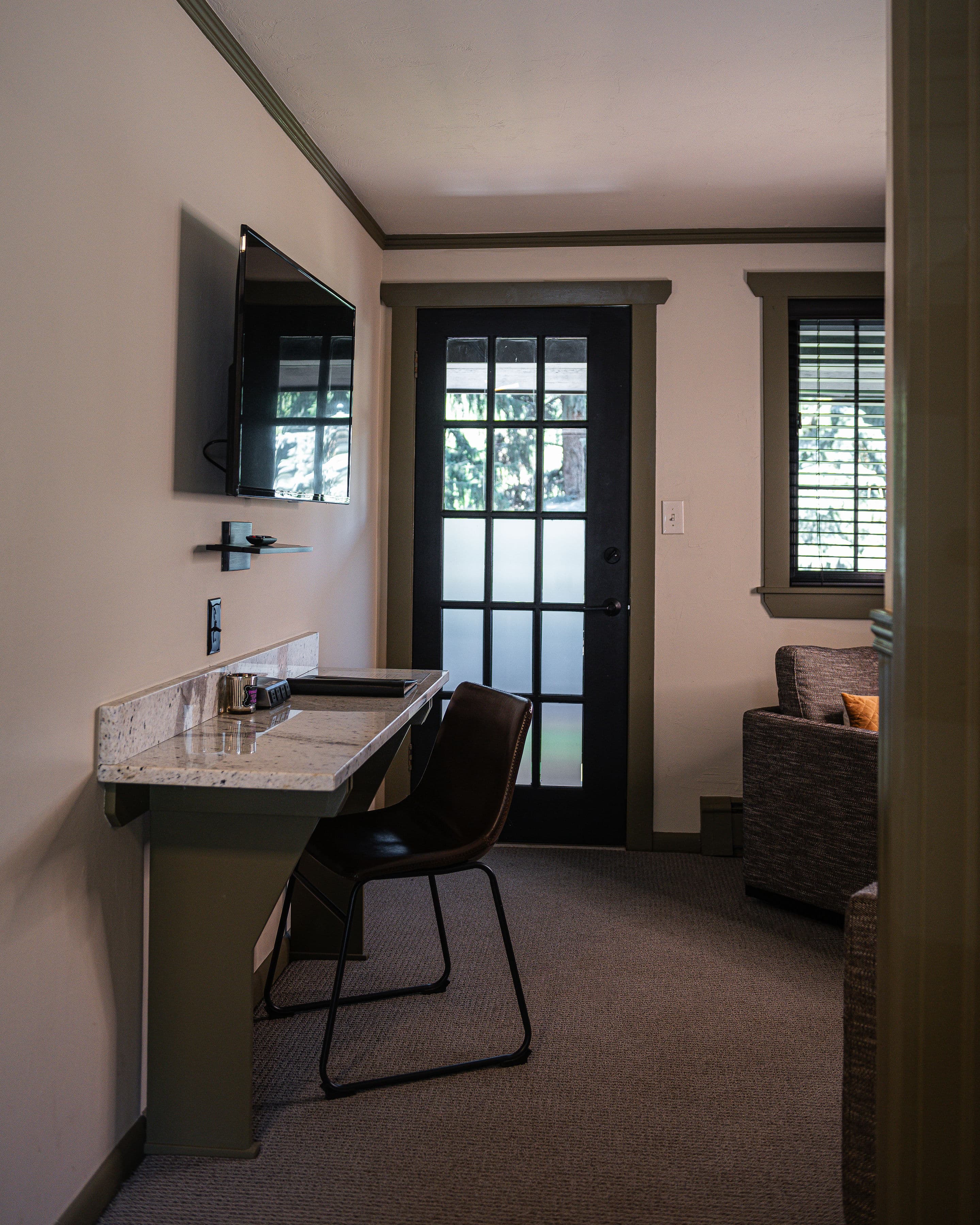 A cozy interior space featuring a desk, chair, television, and a door leading outside.