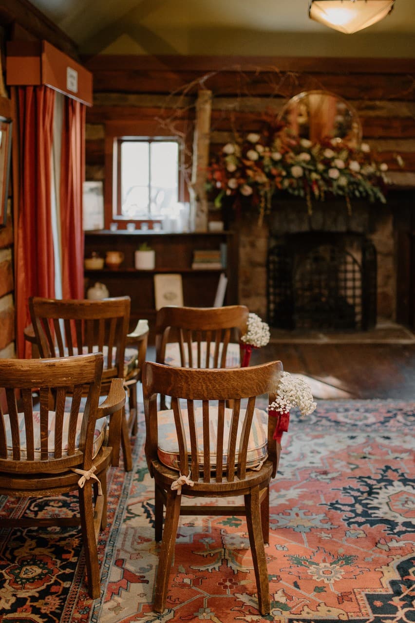 A cozy interior with wooden chairs arranged in front of a stone fireplace, adorned with floral decor.