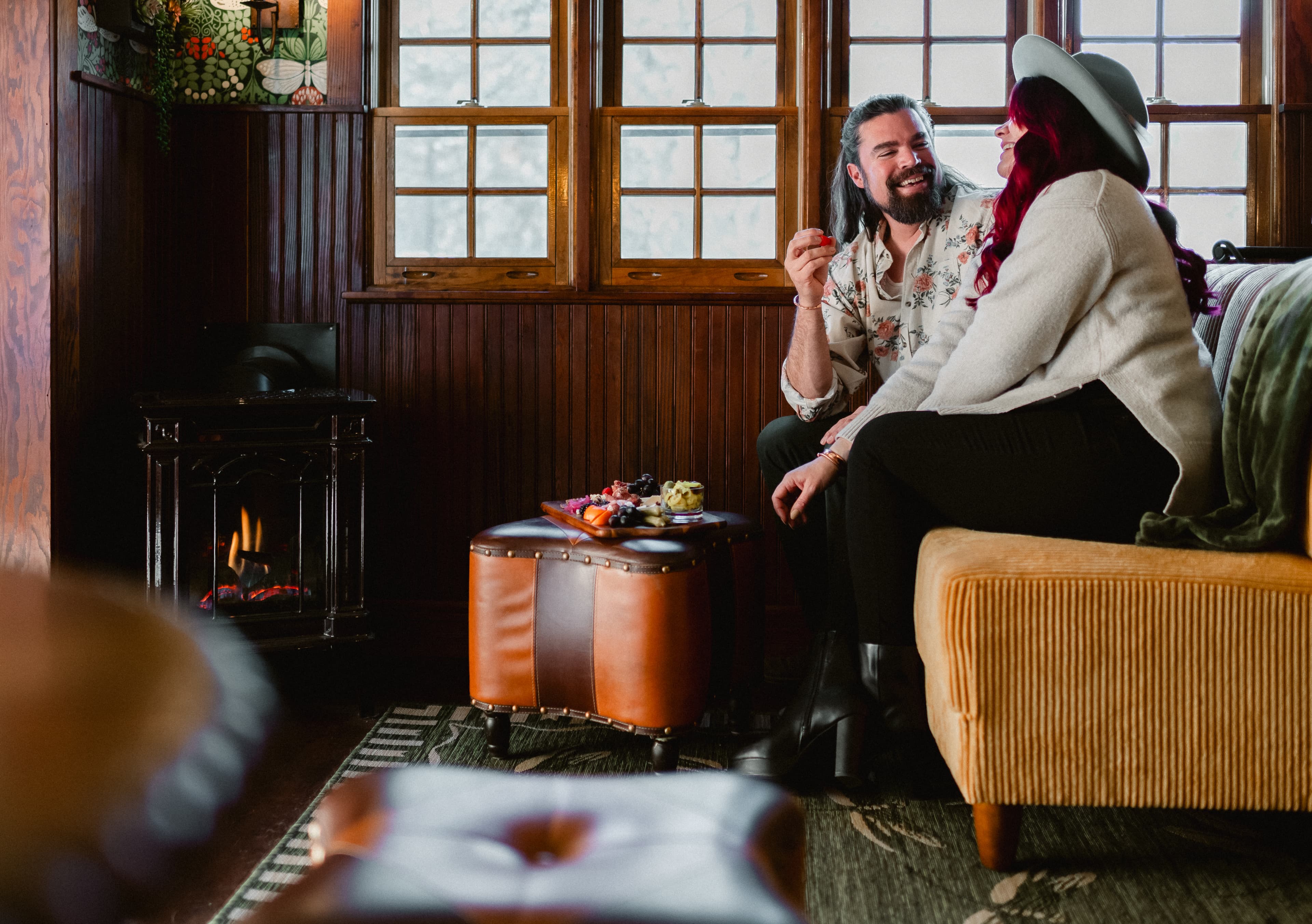 A smiling couple sits together on a couch in a cozy, warmly lit room.
