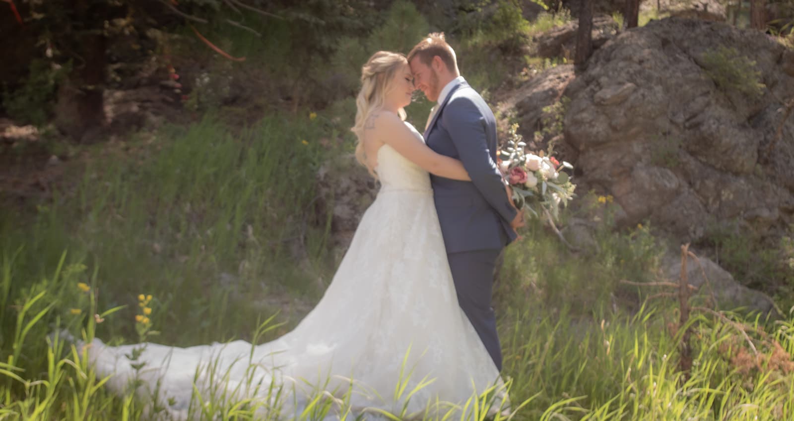 A couple in wedding attire embraces in a lush, green outdoor setting.