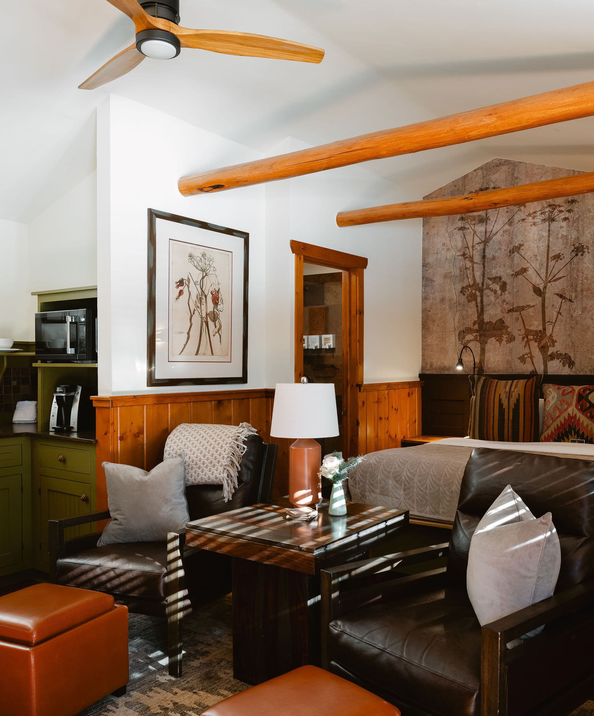 Cozy living area with leather seating, a warm wood aesthetic, and a nature-themed artwork. A ceiling fan adds to the calm, inviting ambiance.