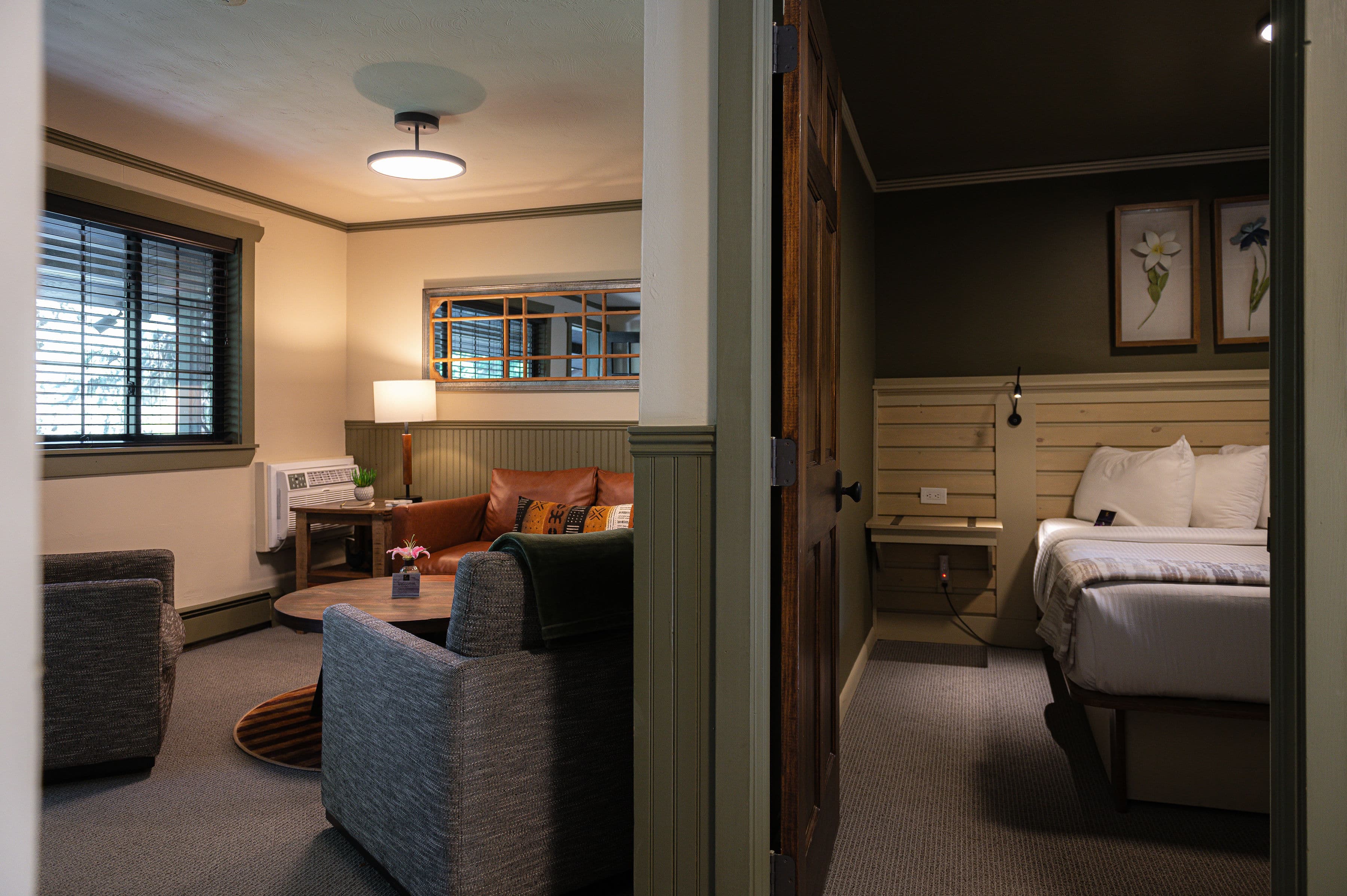 A cozy hotel room featuring a sitting area with armchairs, a coffee table, and a bedroom with a bed and decorative art.