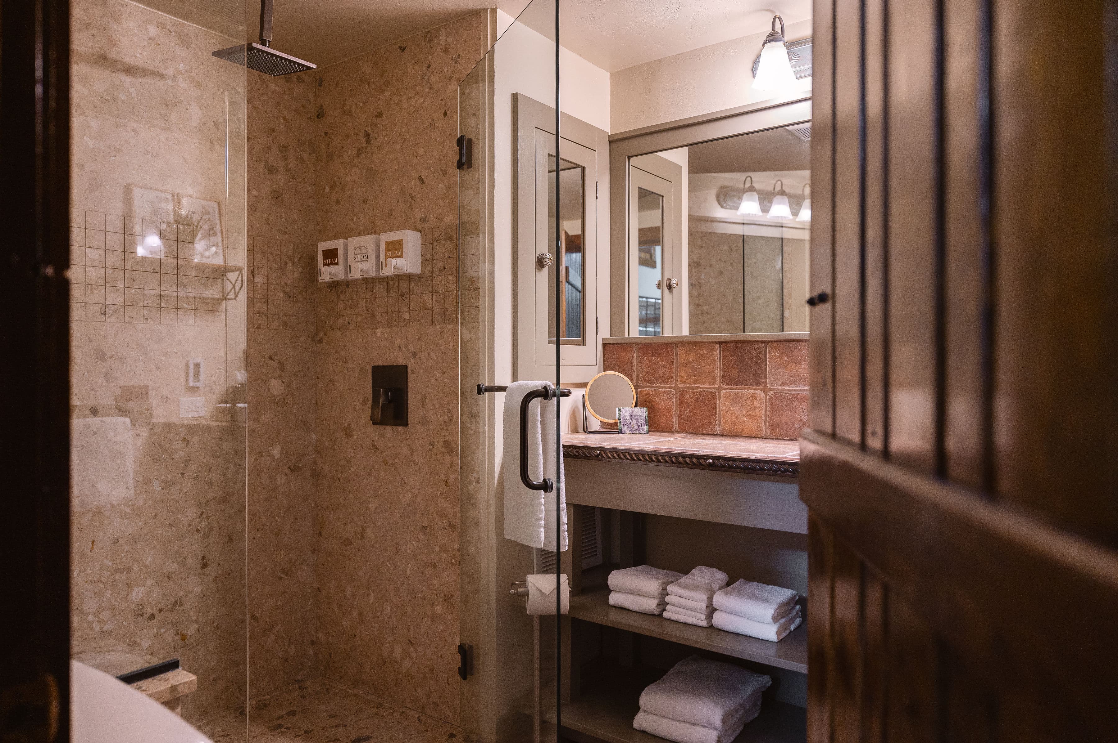 A modern bathroom featuring a glass shower, stone walls, and neatly arranged towels on a shelf.