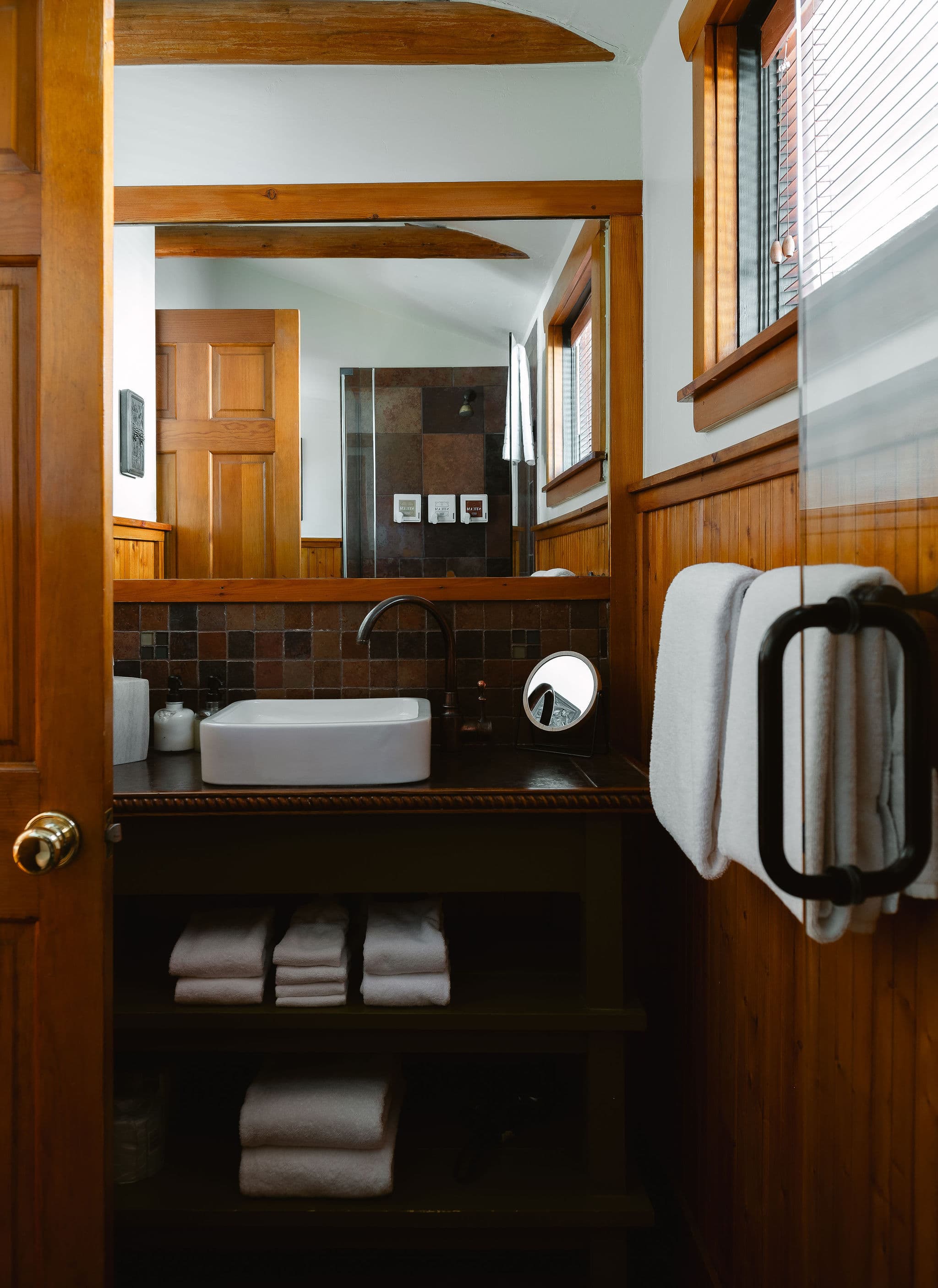 A modern bathroom with wooden accents features a sleek sink, towels, and a mirror.