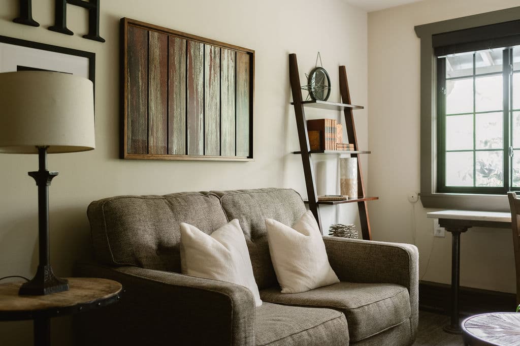 A cozy living room featuring a sofa with pillows, a wooden ladder shelf, and a large window.
