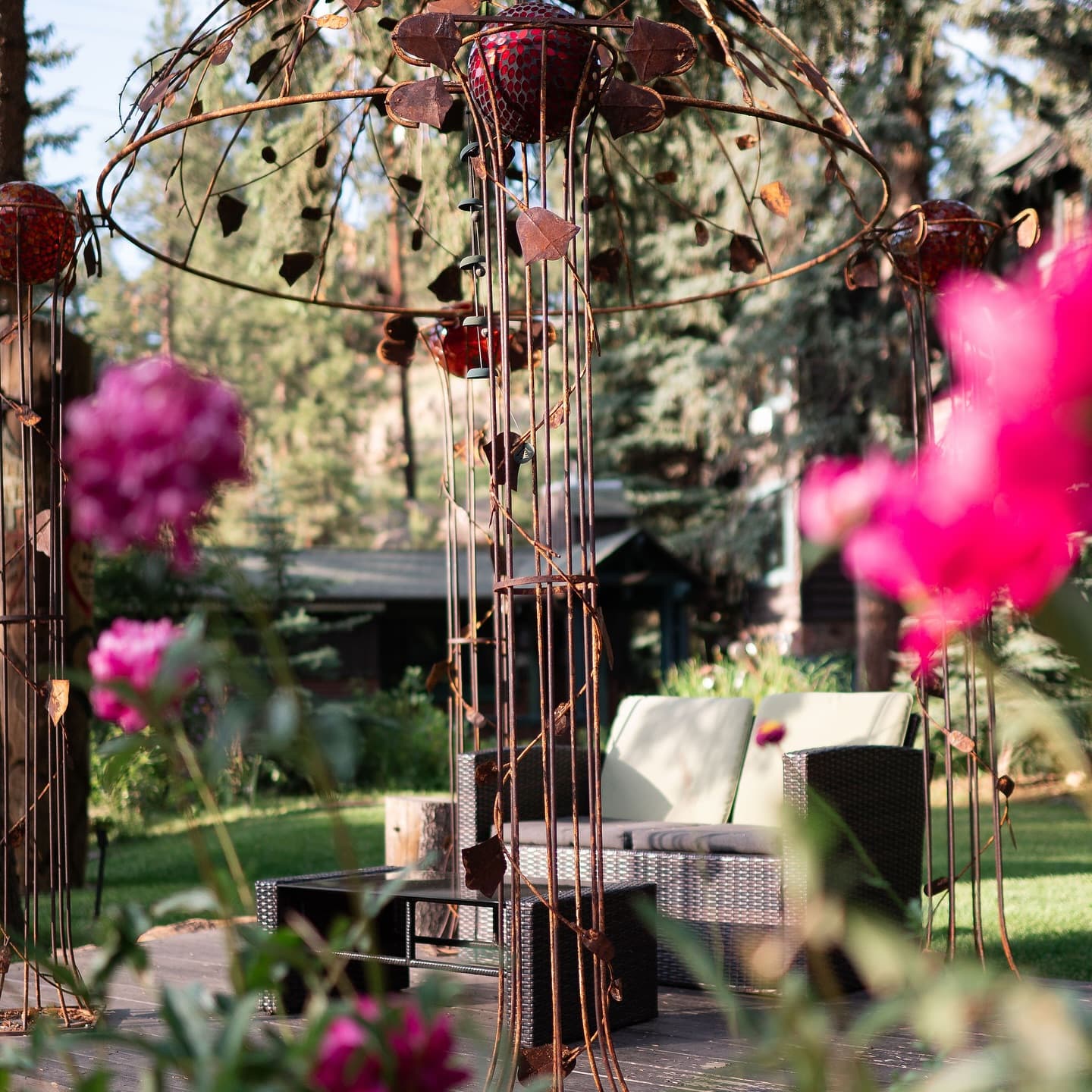 A decorative metal structure surrounded by vibrant flowers and outdoor seating in a lush garden.