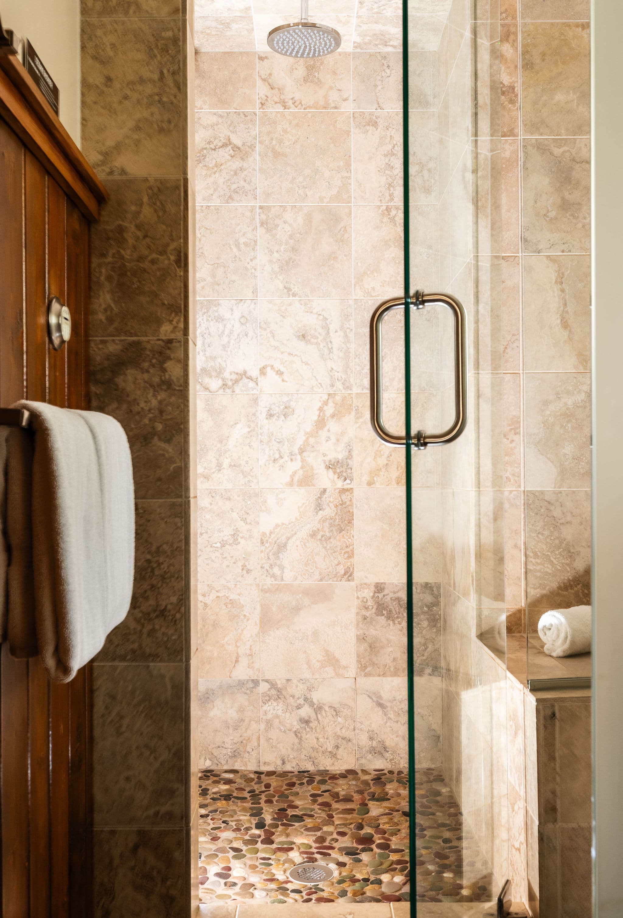 A modern glass shower with stone tile flooring and a towel hanging nearby.