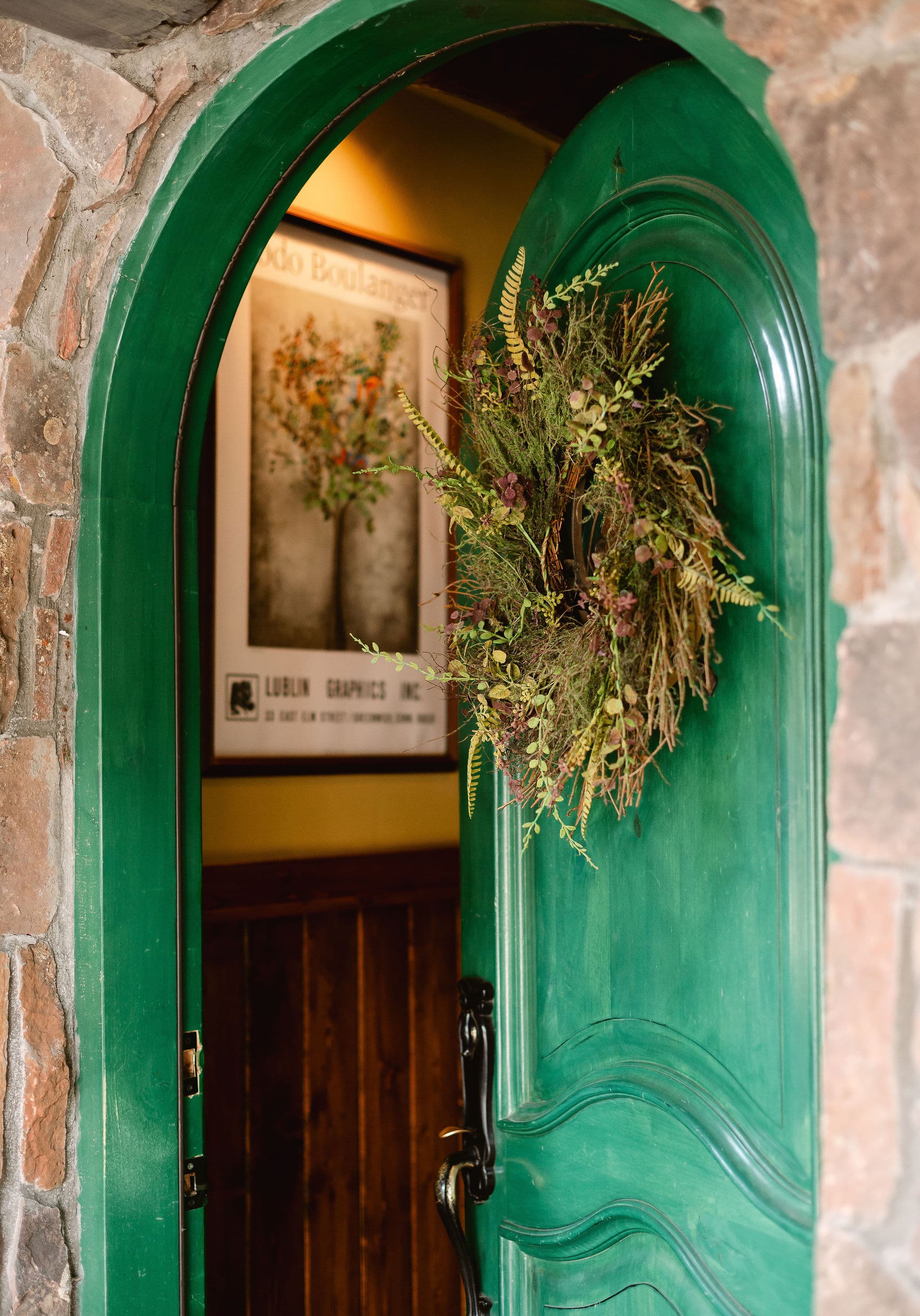 A vibrant green door with a wreath welcomes you into a warmly lit interior featuring framed artwork.
